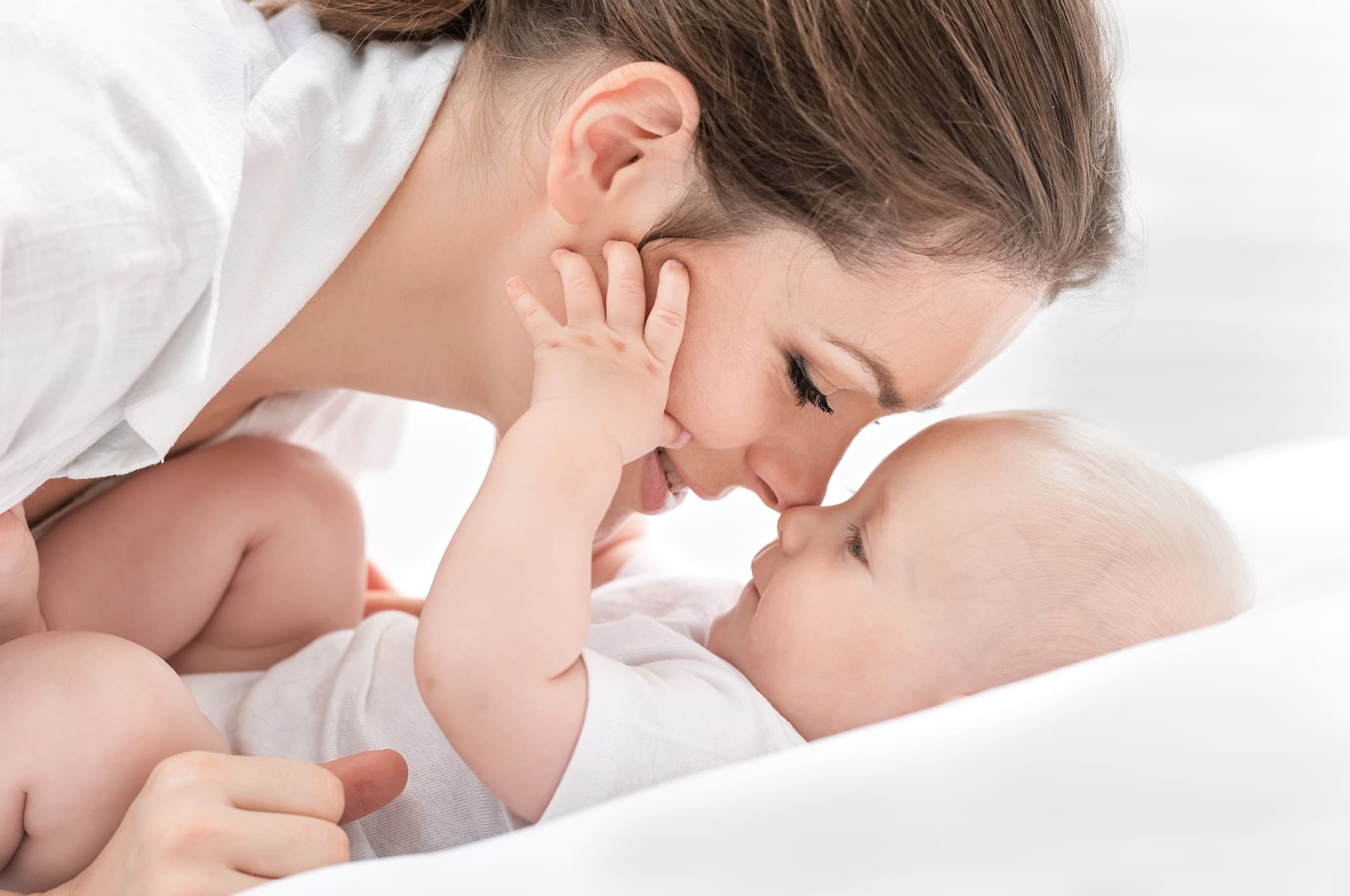 Eine Mutter berührt sanft mit ihrer Nase das Gesicht ihres Babys, während beide liebevoll und glücklich lächeln.